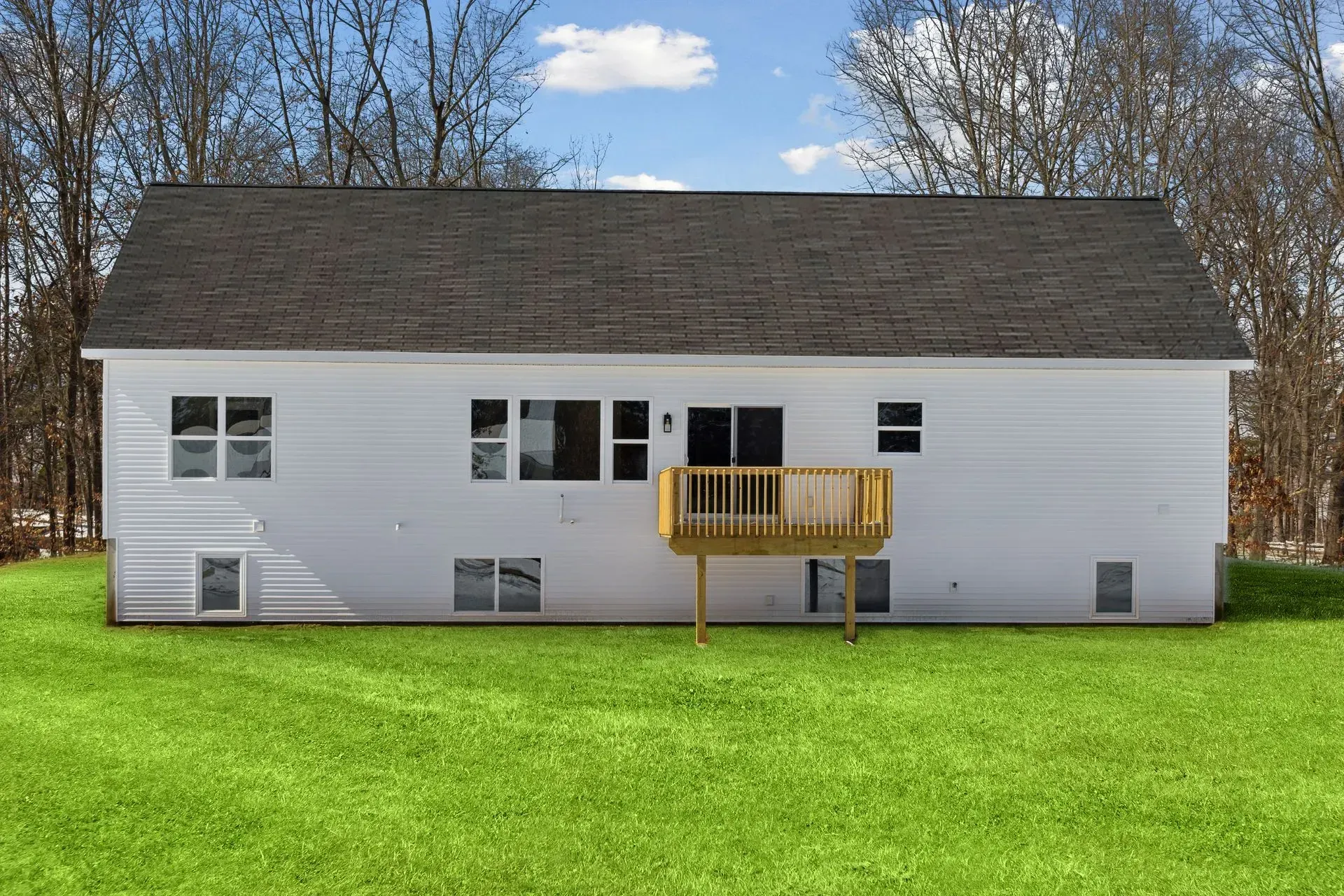 White house with dark roof and small wooden deck in a grassy backyard under a blue sky