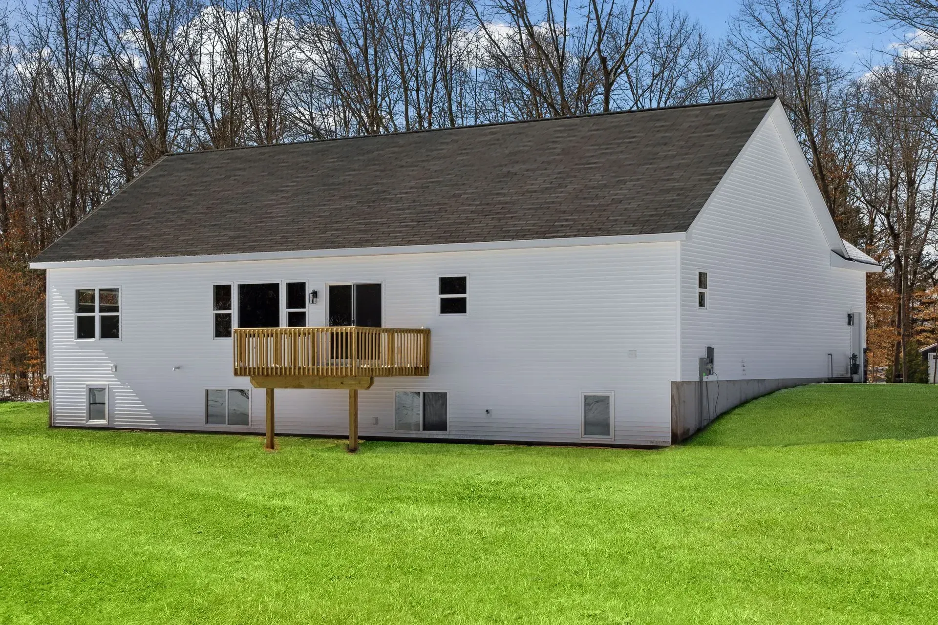 White house with a small wooden deck on a bright green lawn, backed by leafless trees.