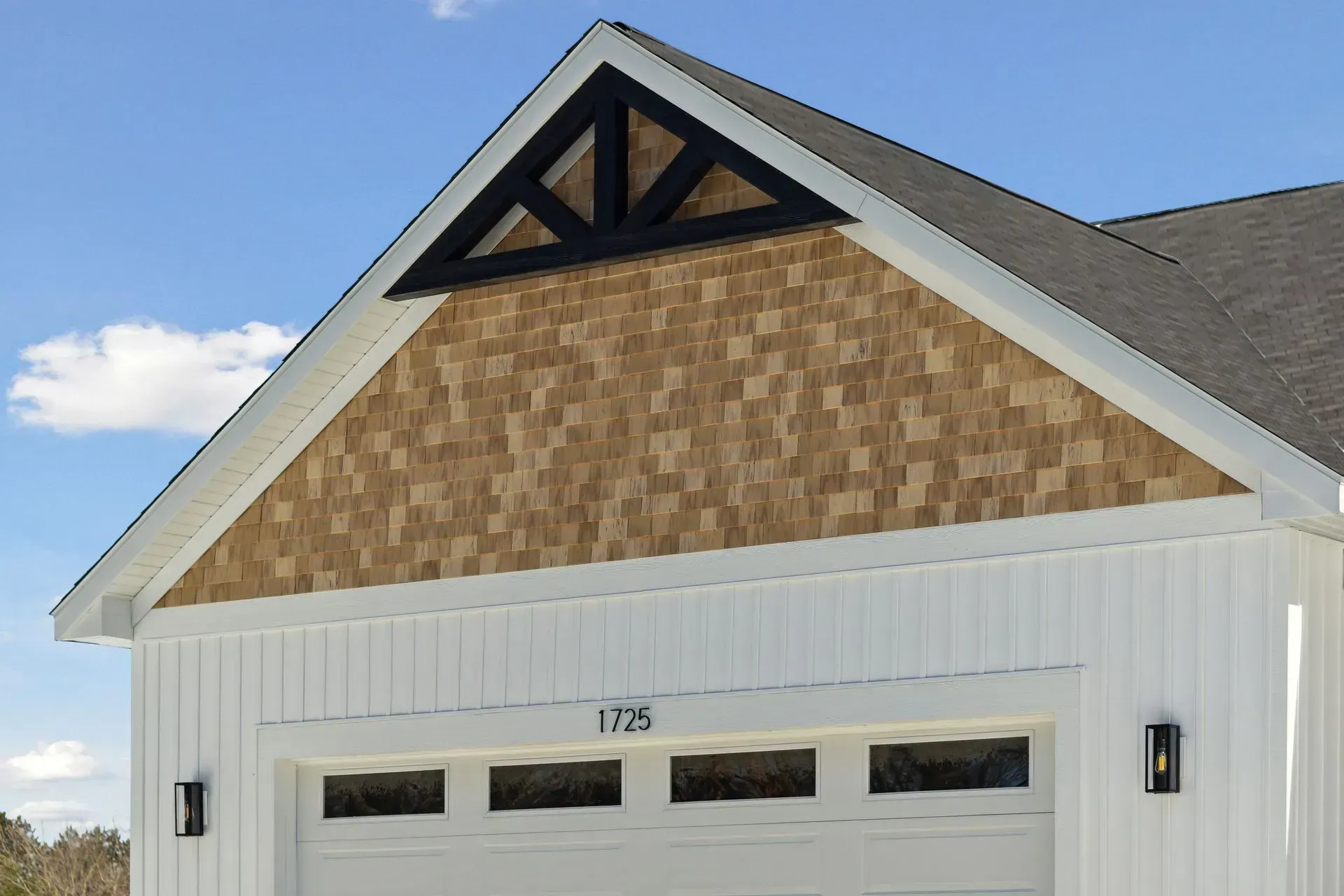 Front of a white garage with tan shingle gable, gray roof, and black trim under a blue sky