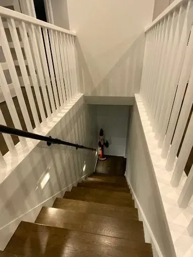 Staircase with white railings and wooden steps, viewed from the top looking down into a narrow hallway.