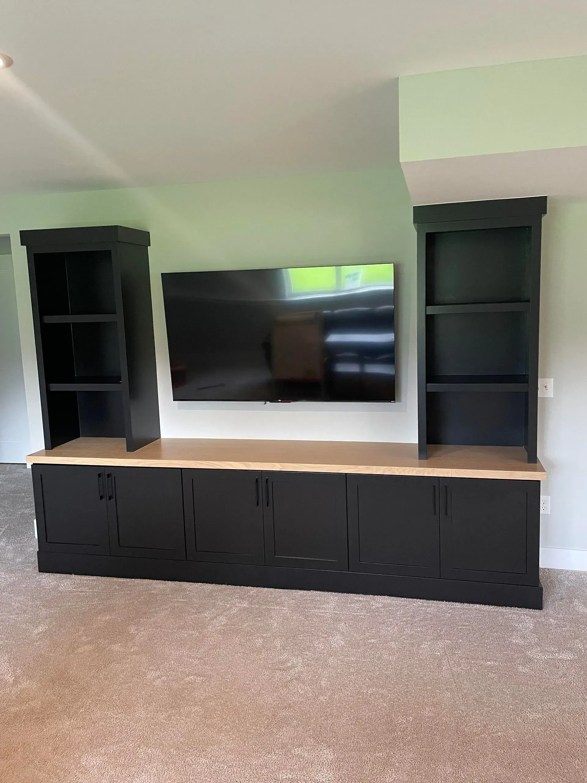 Black entertainment center with TV, shelves, and cabinets against a light green wall in a carpeted room