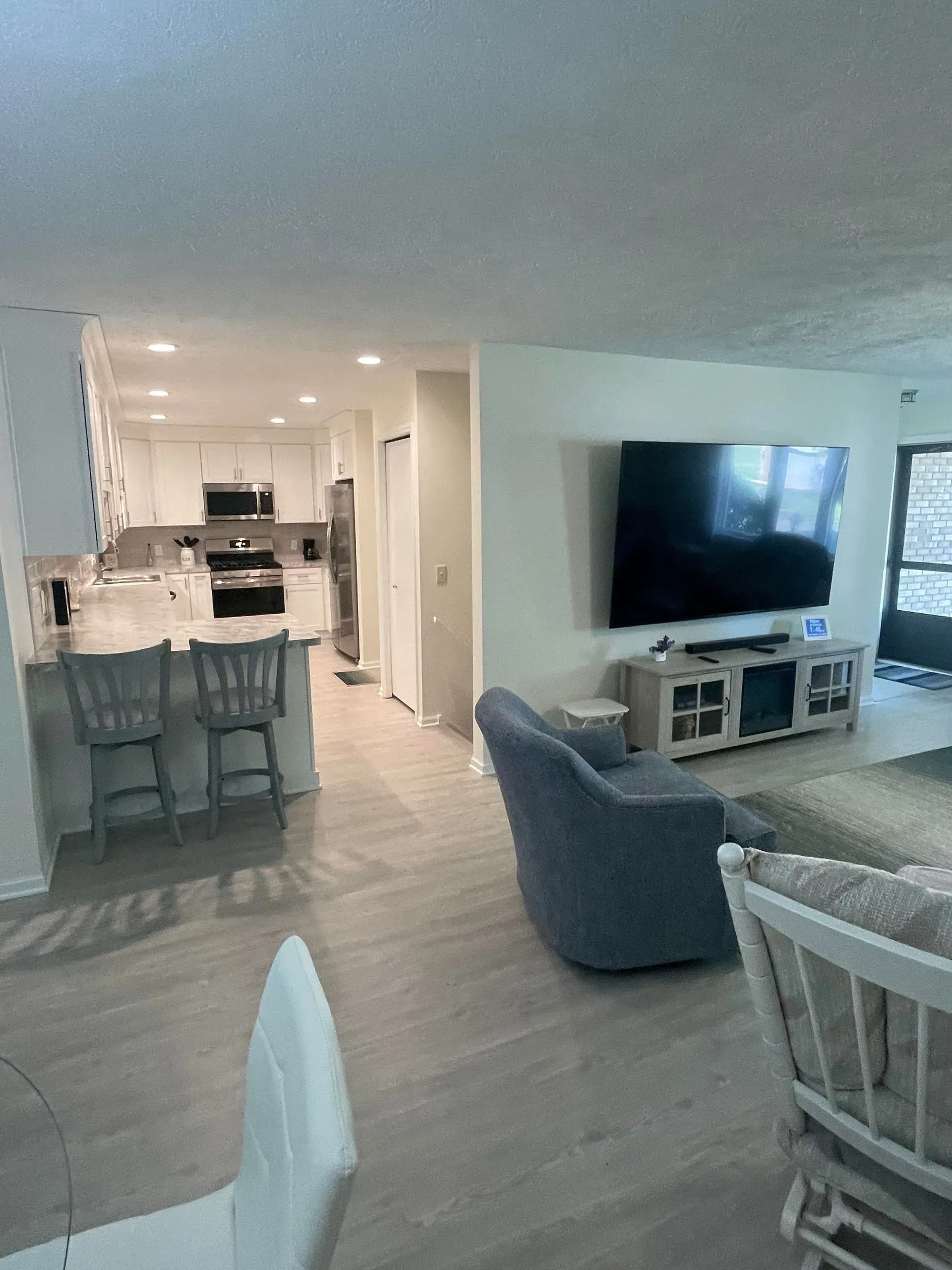 Open-concept living room and kitchen with gray chairs, a large TV, and tiled floors