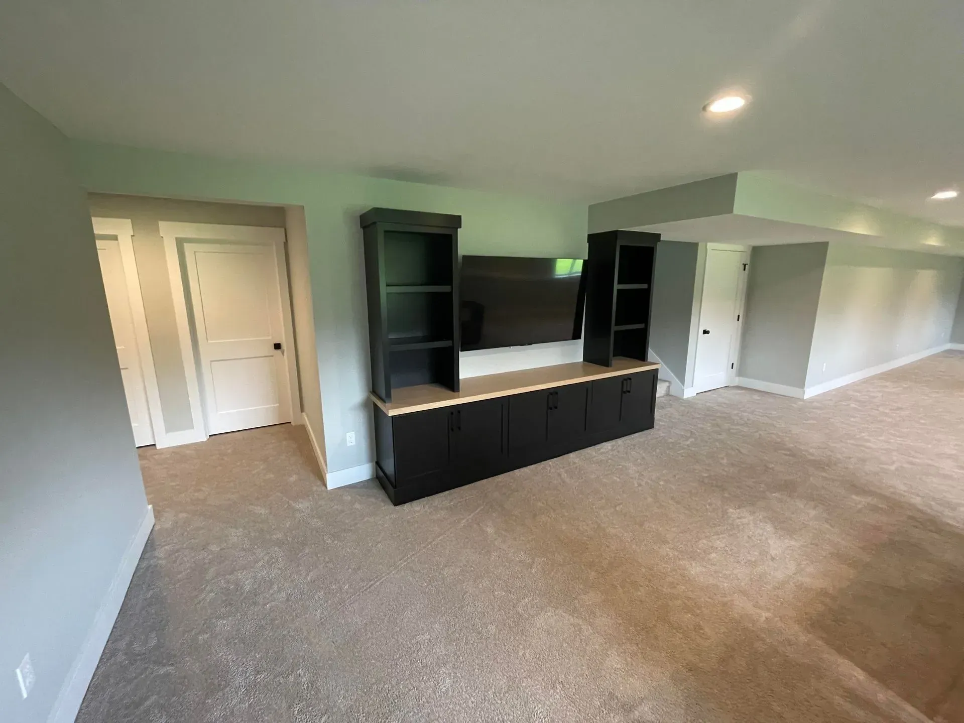 Empty carpeted living room with black built-in entertainment center and white double doors.