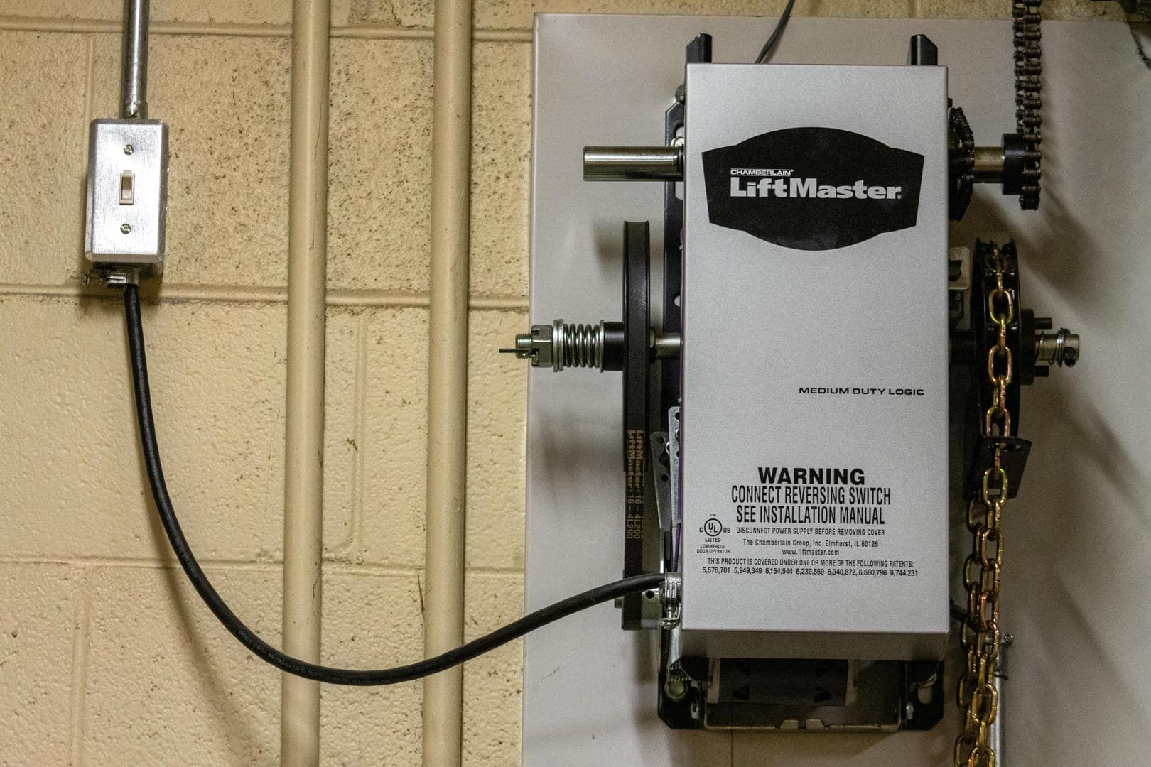 LiftMaster garage door opener mounted on a concrete wall, with wiring and electrical outlet.