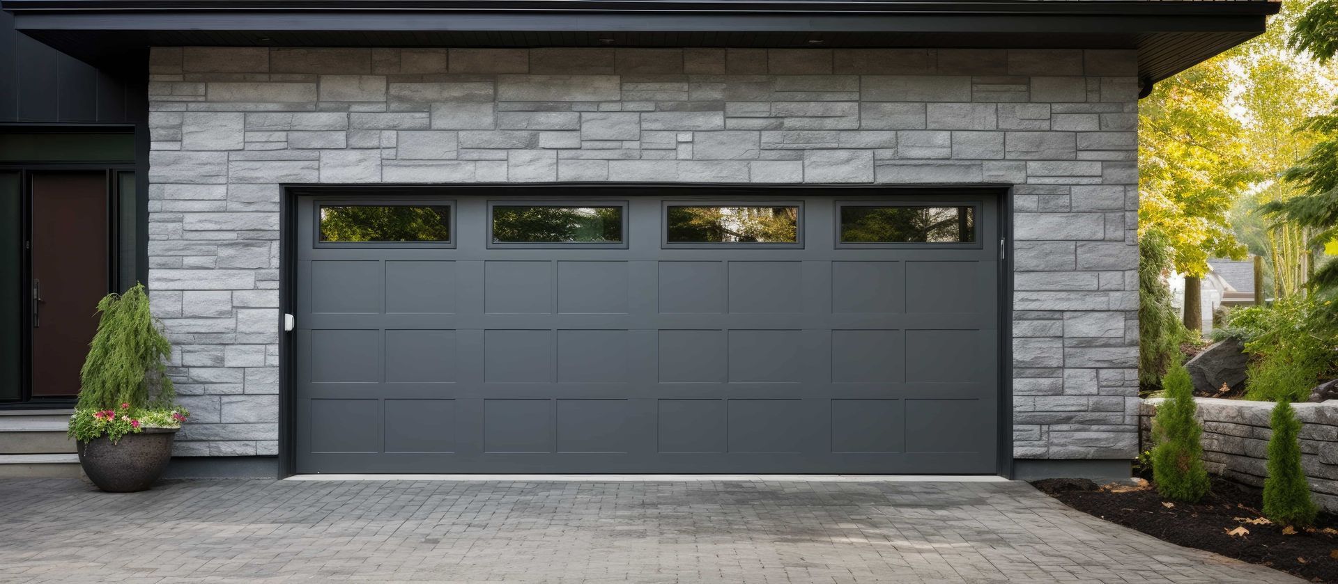 Gray garage door with rectangular windows, set in a stone facade.