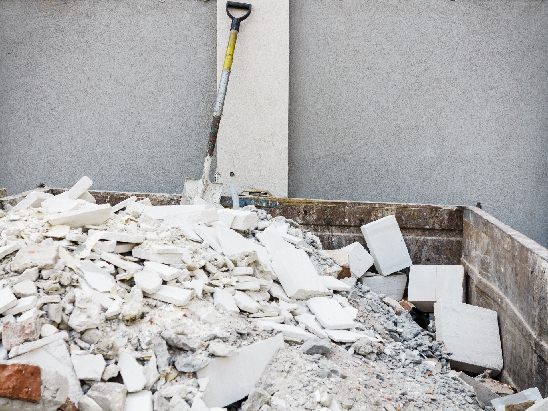 Construction rubble piled beside a wall with a shovel leaning in the corner.