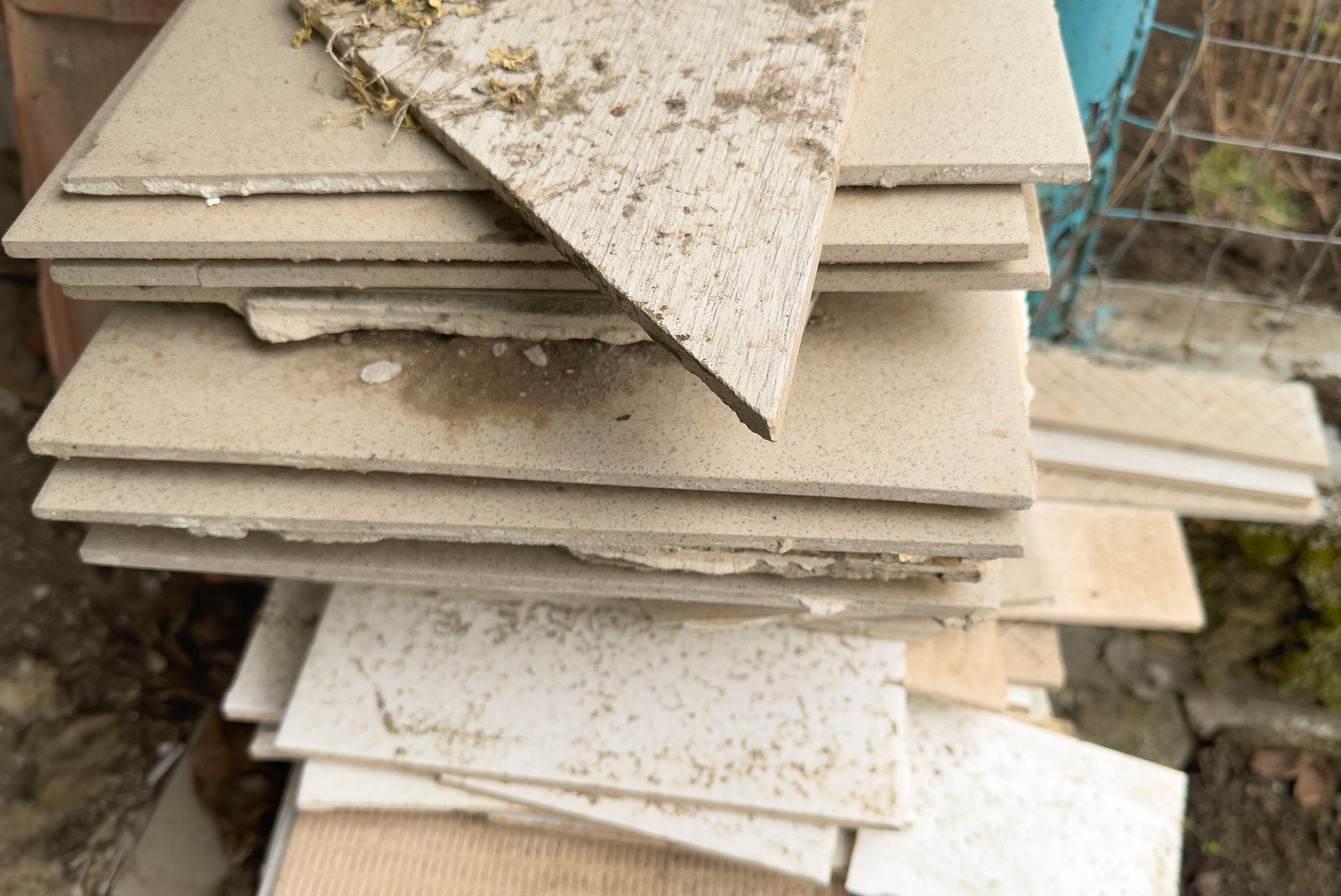 Stack of beige ceramic tiles outdoors, some dusty and chipped