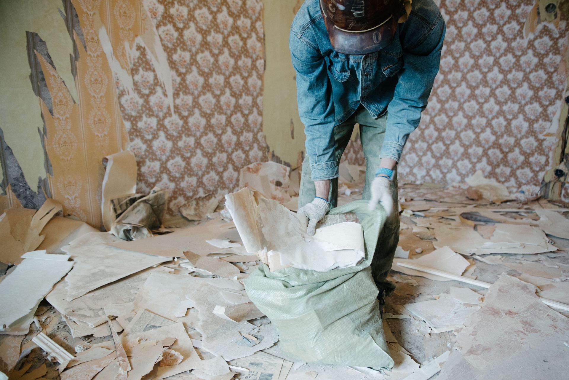 Person tearing out drywall in a damaged room, with debris covering the floor