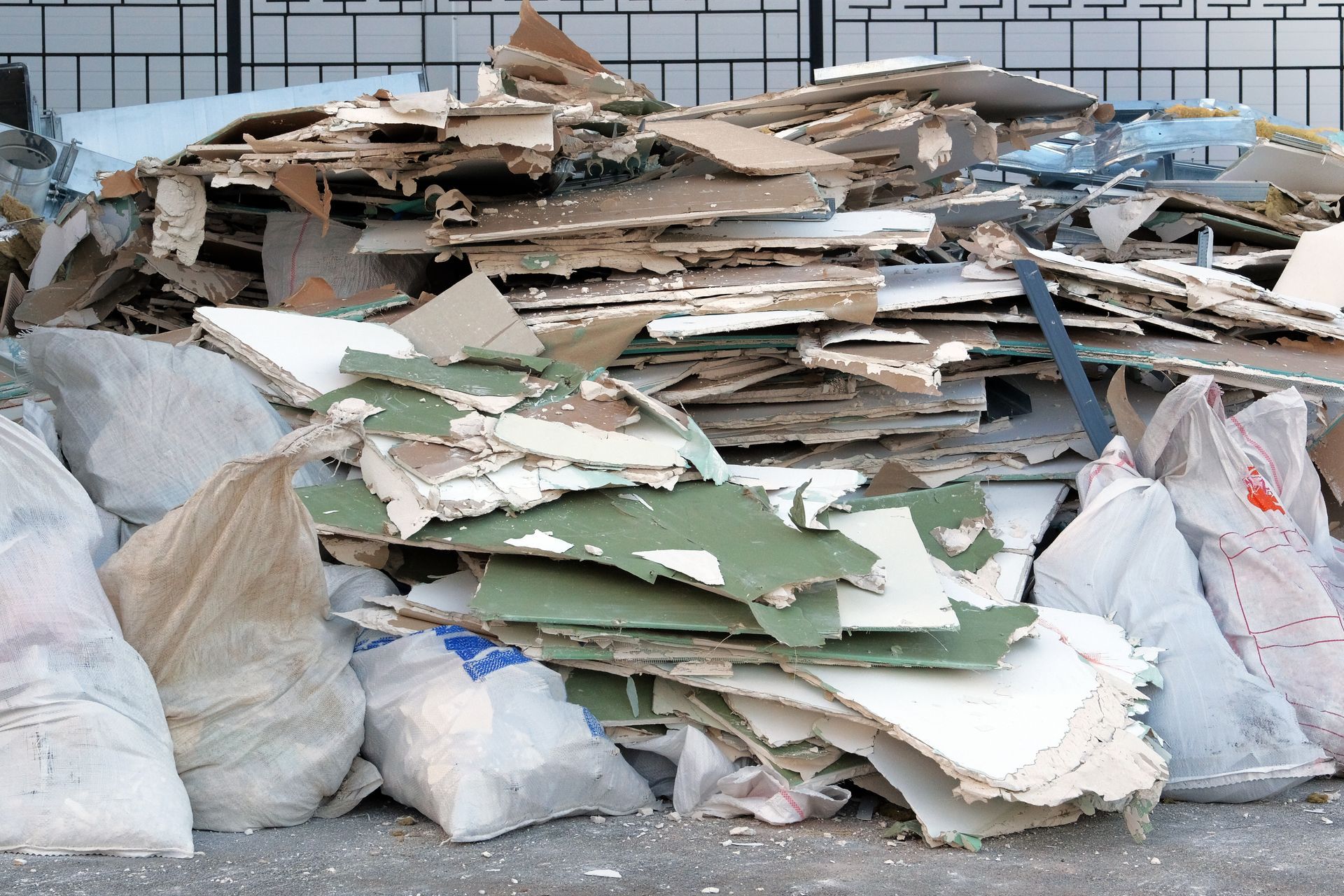 Pile of cardboard and mixed debris with white trash bags in an outdoor waste area