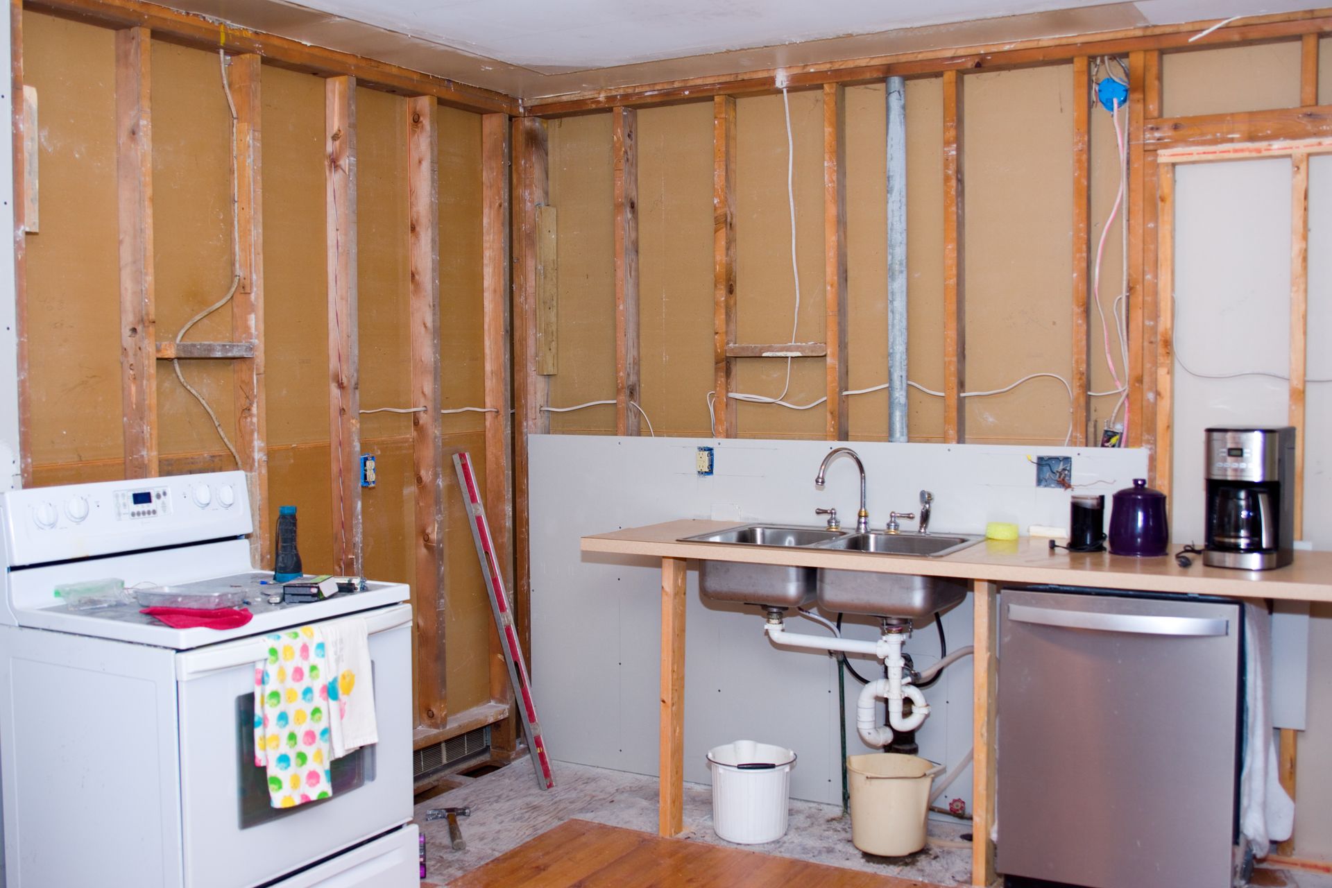 Partially renovated kitchen with exposed studs, stove, sink, and stainless-steel refrigerator