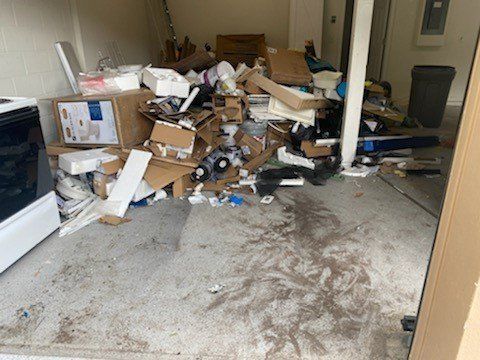 A cluttered room with piles of boxes, debris, and trash scattered across the floor and shelves.