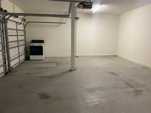 Empty garage with concrete floor, white walls, a support post, and a stove against the left wall.