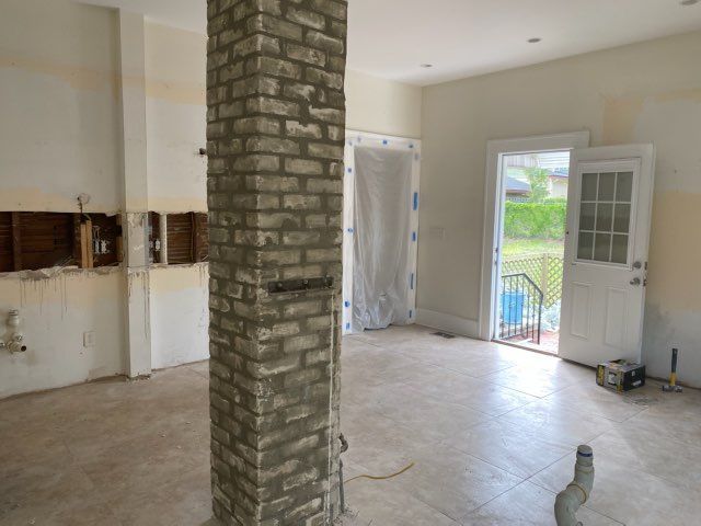Empty room under renovation with exposed brick column, white walls, and open door to a patio.