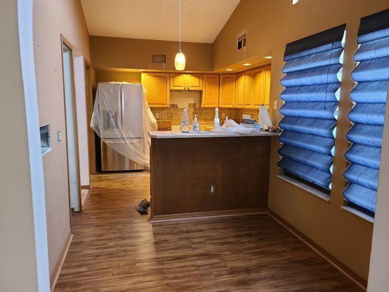 Empty kitchen and dining area with brown wood floors, yellow cabinets, and blue window blinds