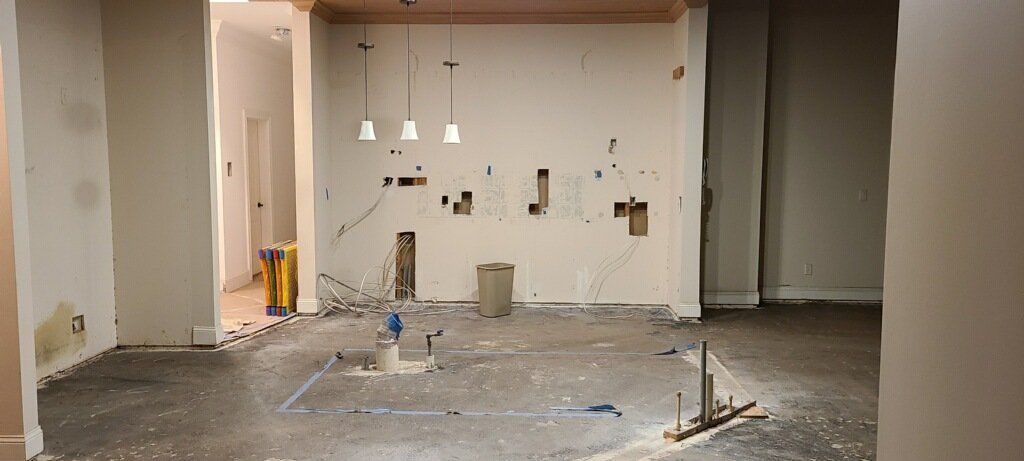 Empty, unfinished room with exposed walls, debris on floor, and hanging lights under construction.