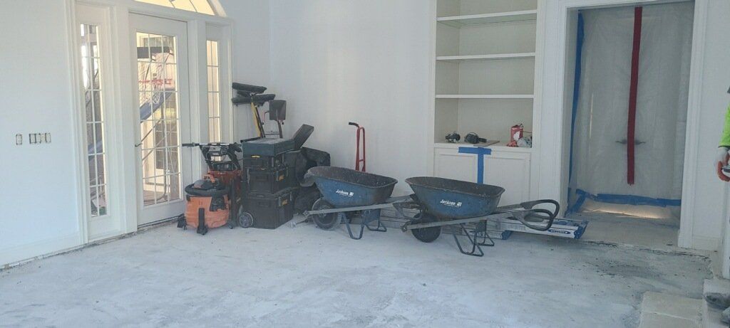 Construction tools and wheelbarrows in a bare interior room with open doors and shelves