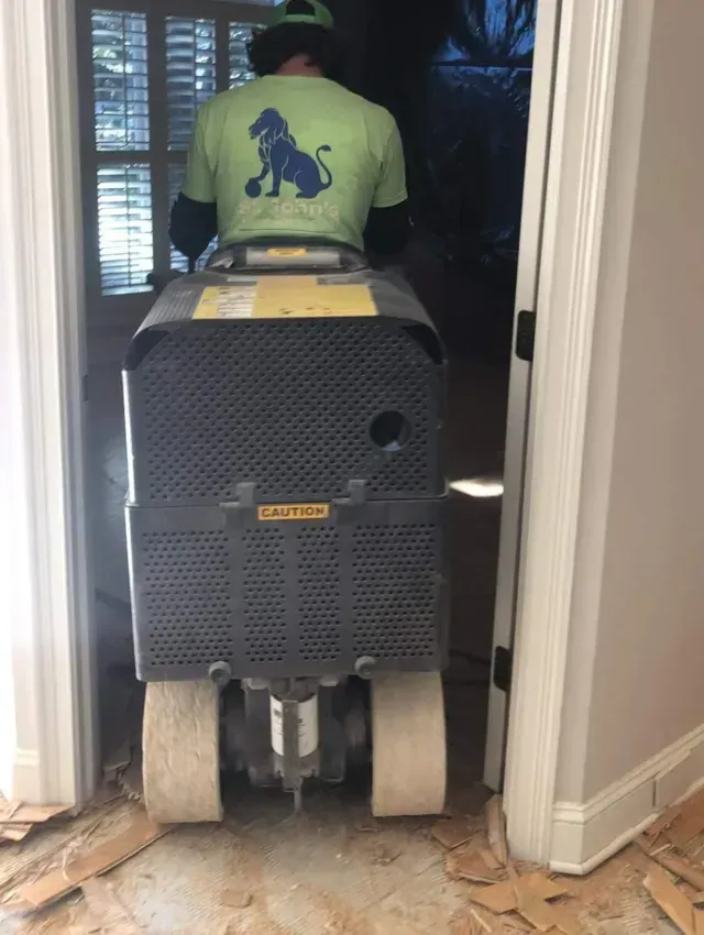 Person on a ride-on floor scrubber in a doorway, with a tiled floor and dim room beyond.