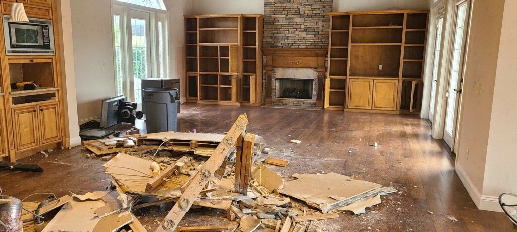 Damaged living room with shattered drywall, debris on the floor, and empty built-in shelves exposed to the wall