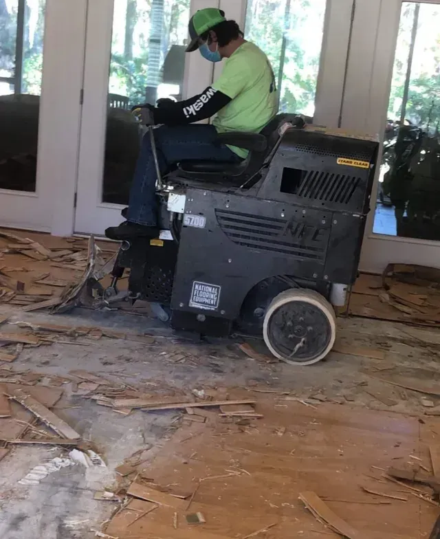 Person in a green shirt and helmet sits on a mobility scooter amid debris inside a damaged building.