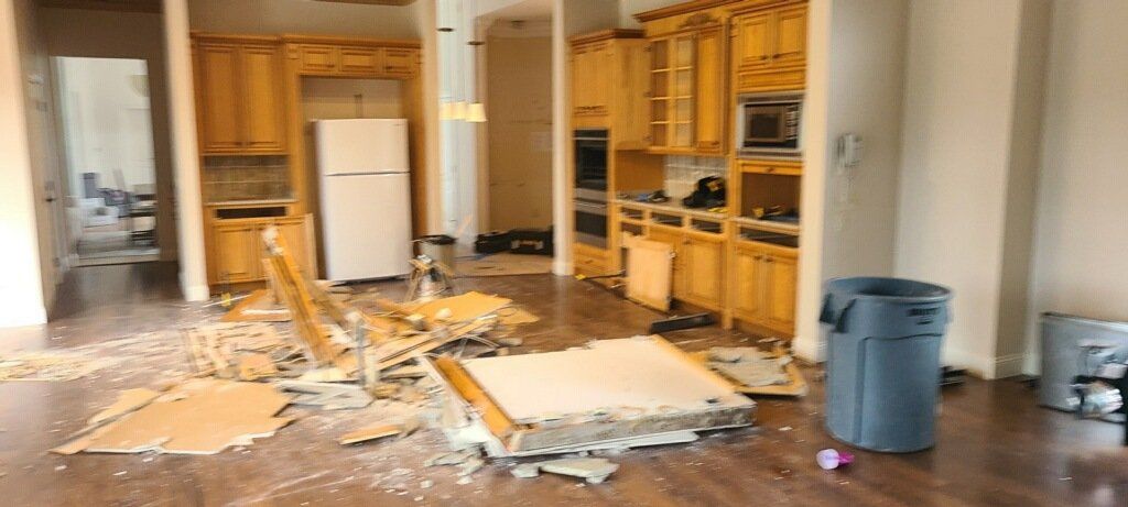 Damaged kitchen with debris scattered across the floor and cabinets along the back wall