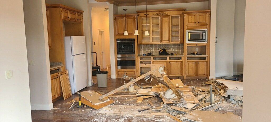 Damaged kitchen with shattered cabinets, debris on the floor, and overturned appliances amid heavy damage.