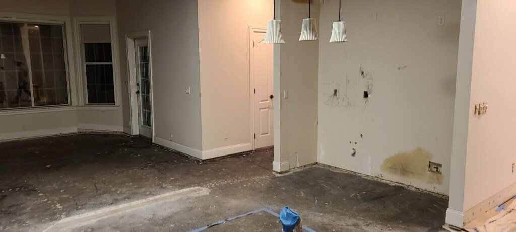 Empty room under renovation with bare walls, hanging lights, and a patchy concrete floor