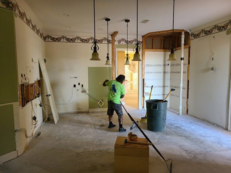 Person using a power tool in a room under renovation, with exposed walls and construction debris.