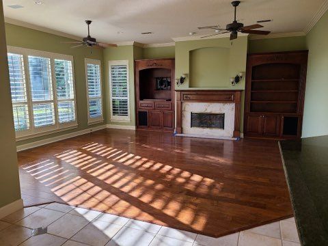 Empty living room with hardwood floor, fireplace, built-in shelves, and sunlight through large windows
