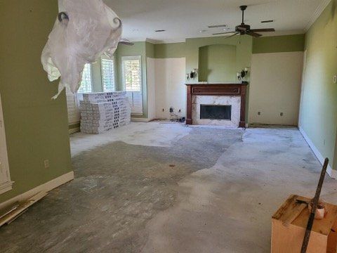 Empty living room under renovation with torn ceiling, fireplace, green walls, and stacked boxes near windows