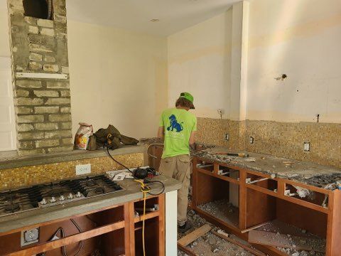 Person working in a kitchen under renovation with unfinished cabinets and exposed countertops.