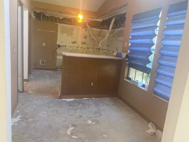 Dusty kitchen under renovation with exposed ceiling, brown cabinets, and blue window blinds