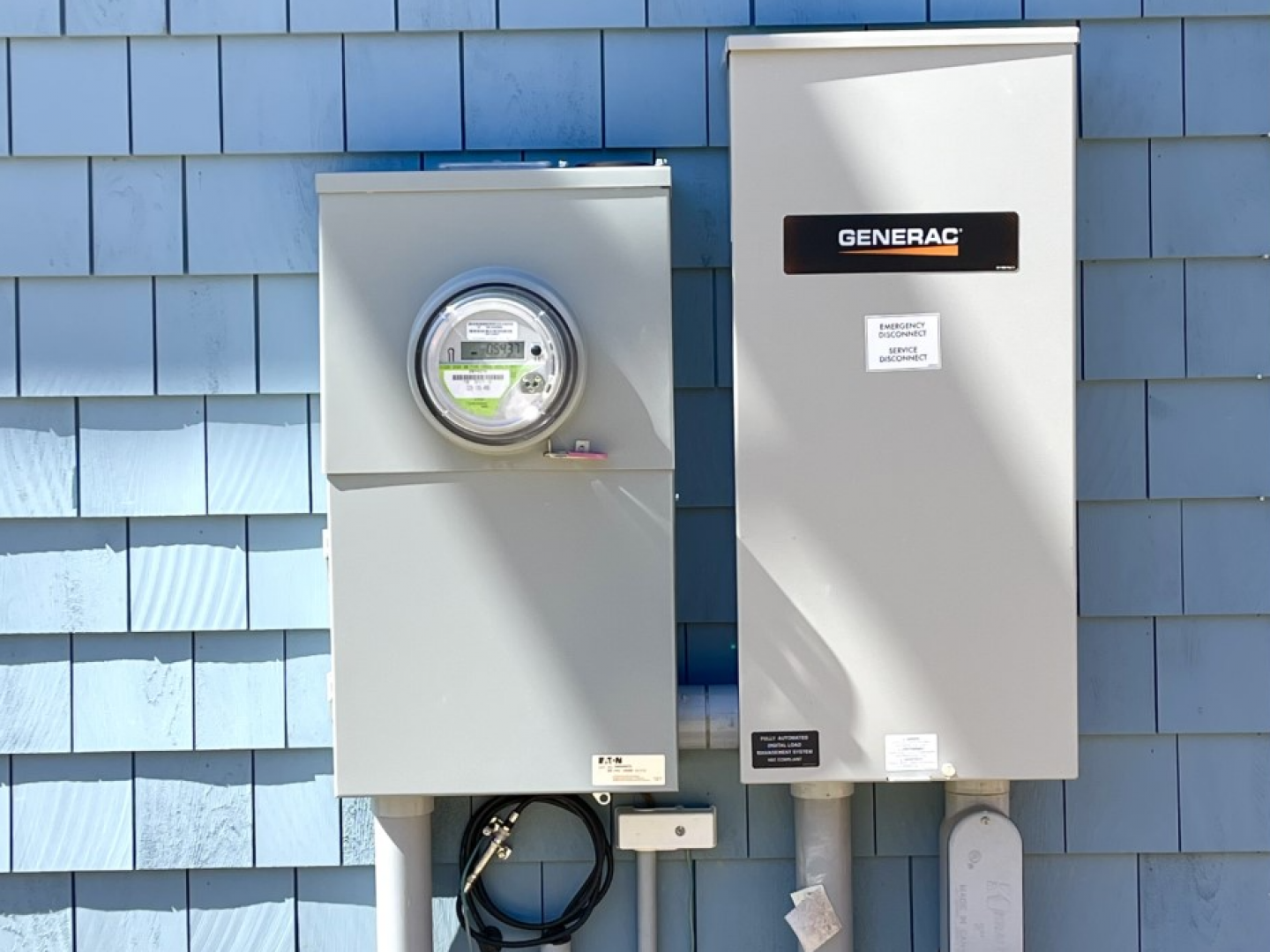 Two gray utility meters mounted on a blue shingled exterior wall