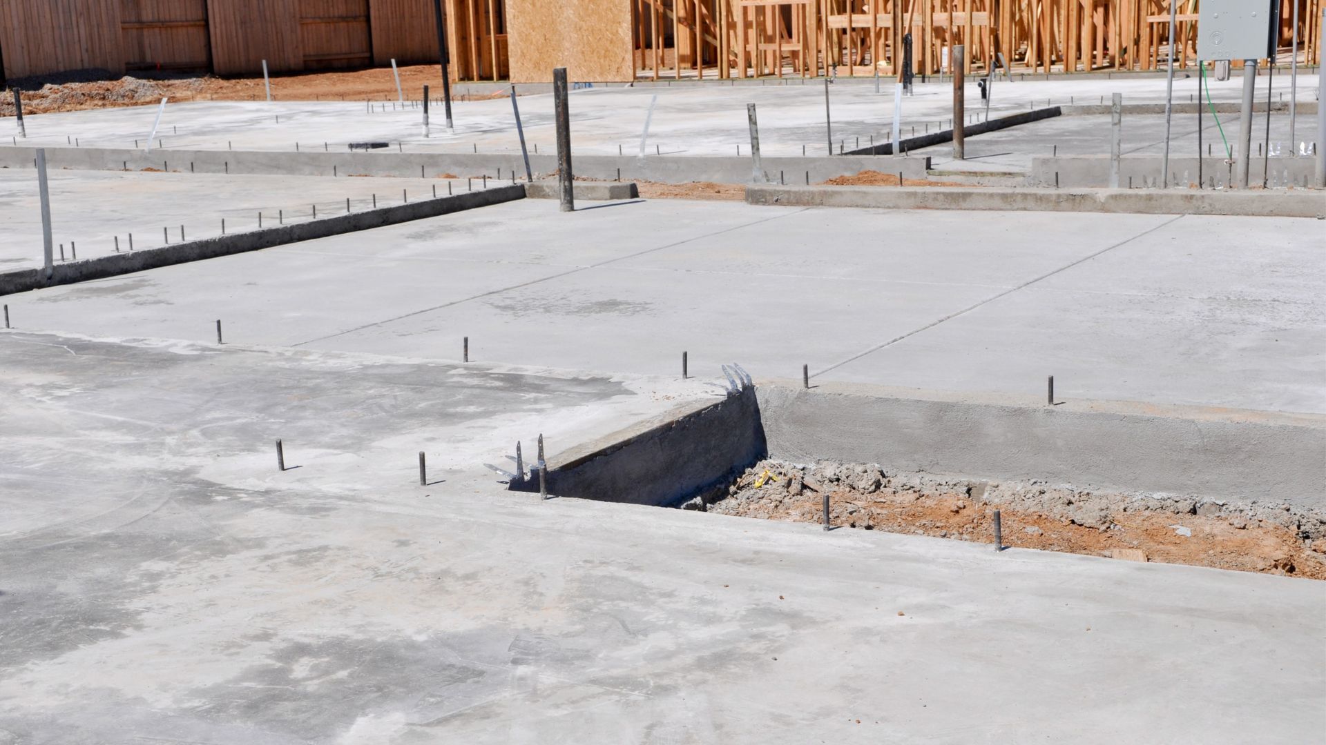 Concrete foundation slab under construction with exposed rebar and wooden framing in the background