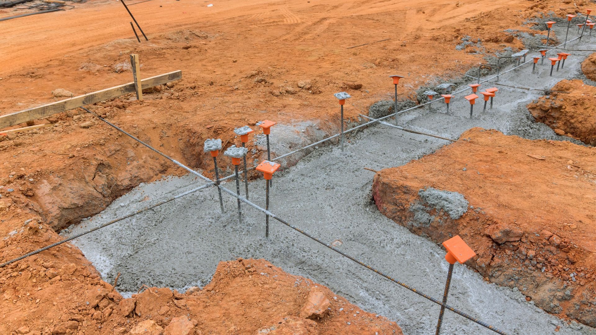 Concrete foundation trenches with rebar and orange markers in a dirt construction site