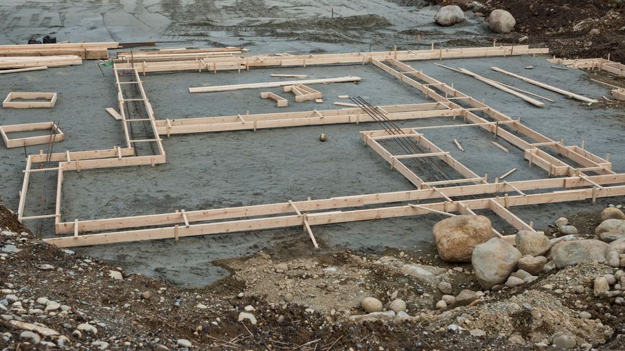 Wooden foundation formwork laid on wet gravel near rocks at a construction site