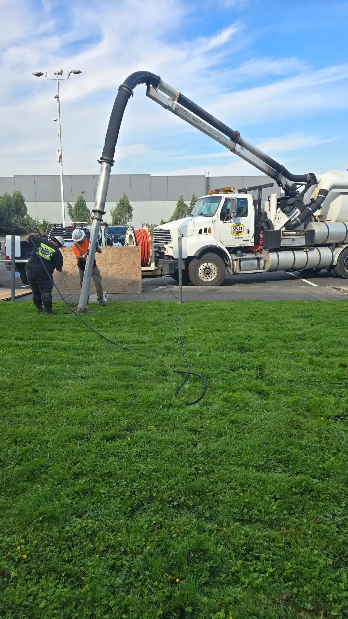 SWAT technicians guiding a galvanized pole into a hydrovac cut hole while the vacuum boom holds position