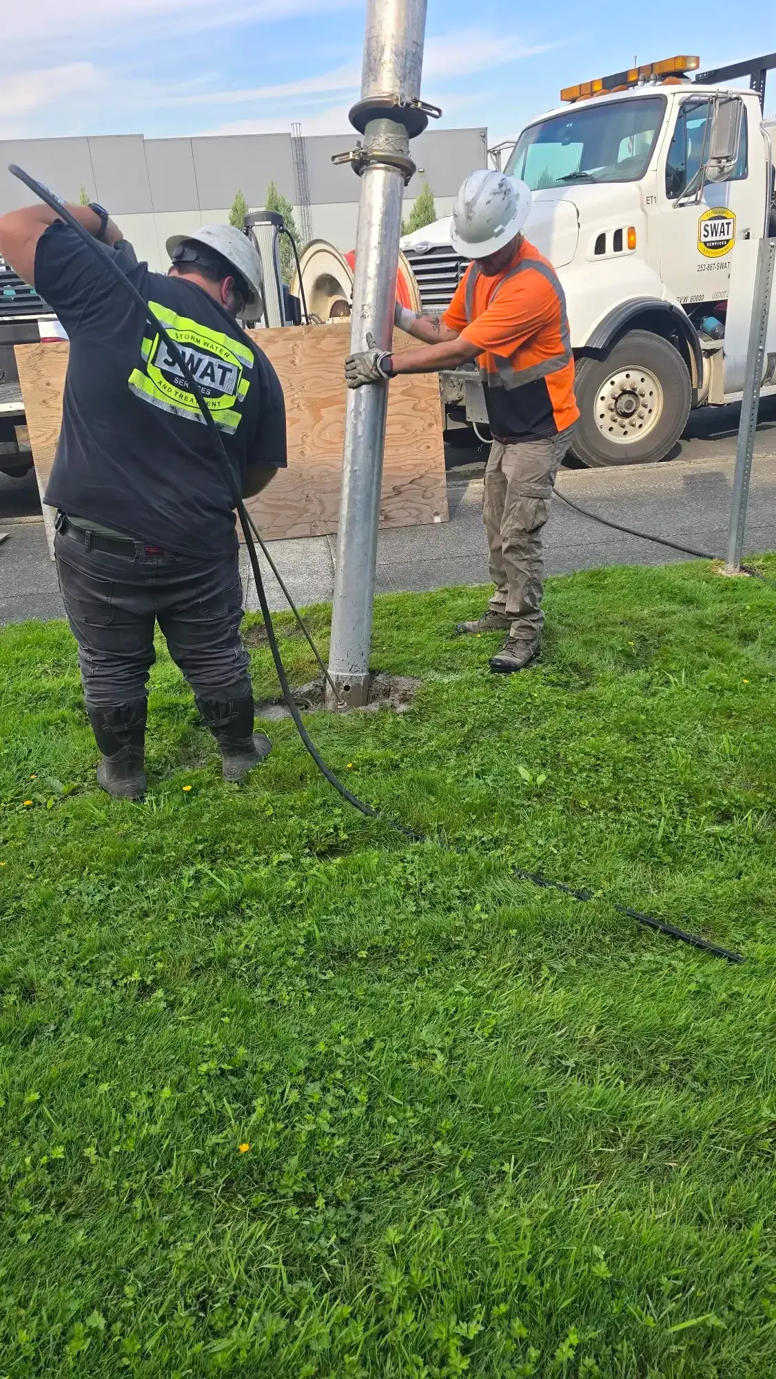 Two SWAT technicians in hard hats setting a pole by hand into a hydro excavated slot in Buckley, WA