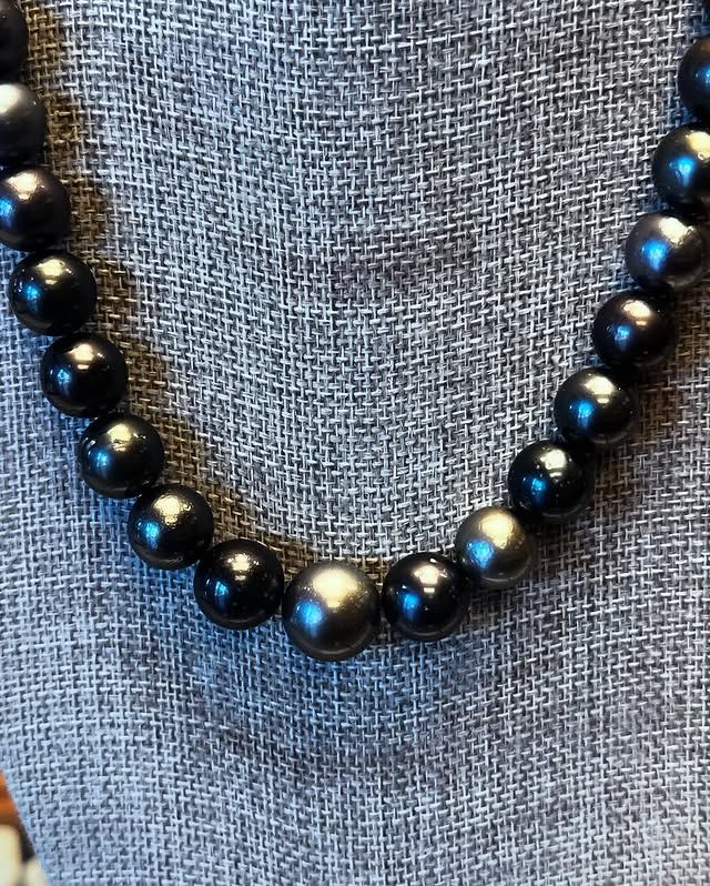 Dark gray beaded necklace on a textured gray background.