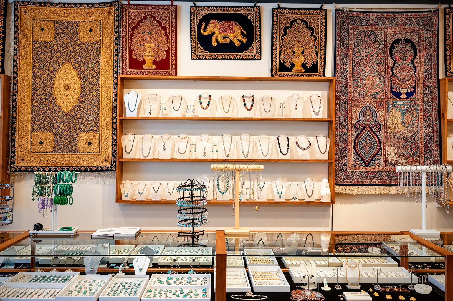 Jewelry store display with necklaces on shelves, rugs on wall, glass display cases.