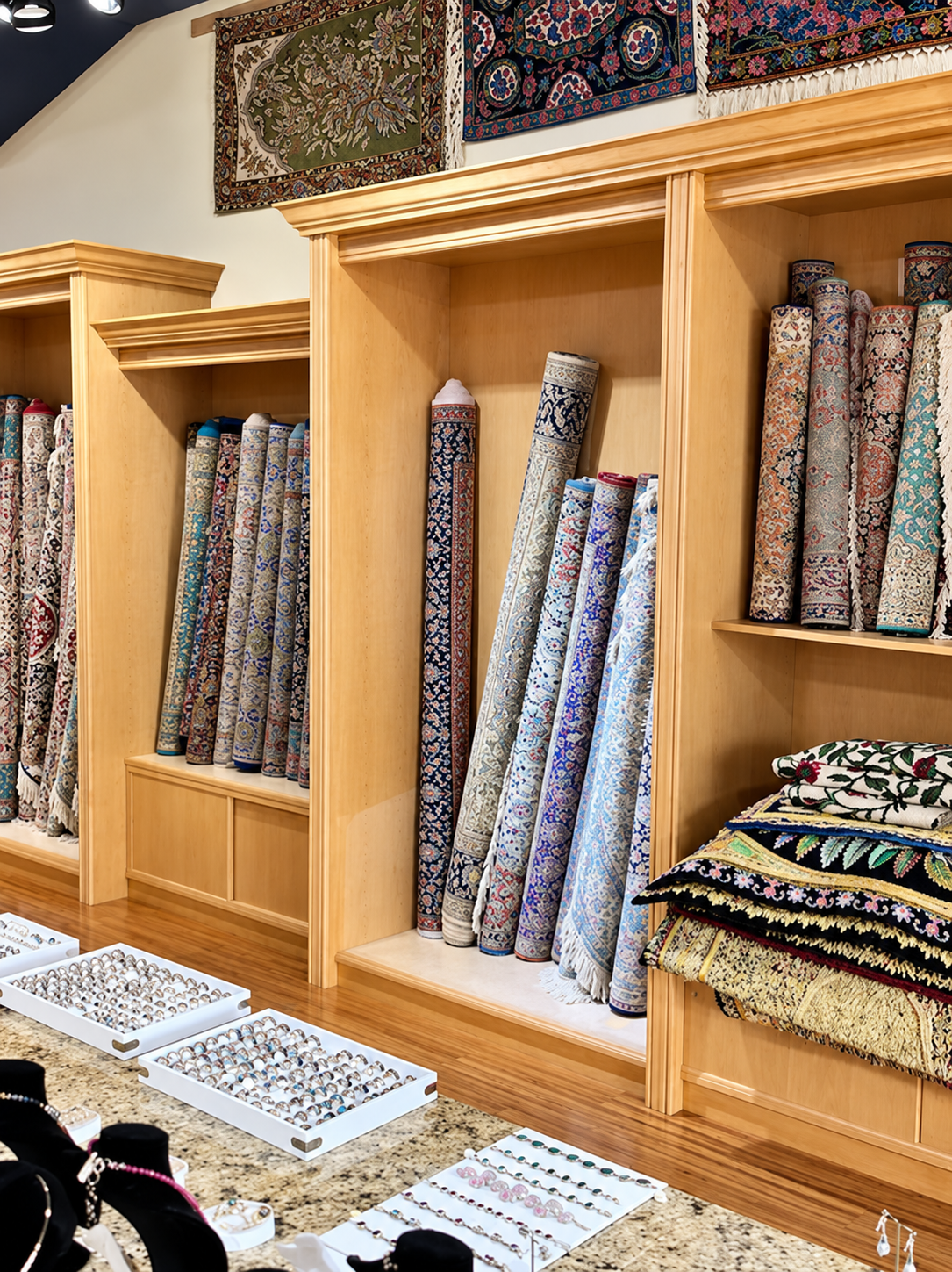 Rug store display with rolled carpets in wooden shelves; several carpets hang above.
