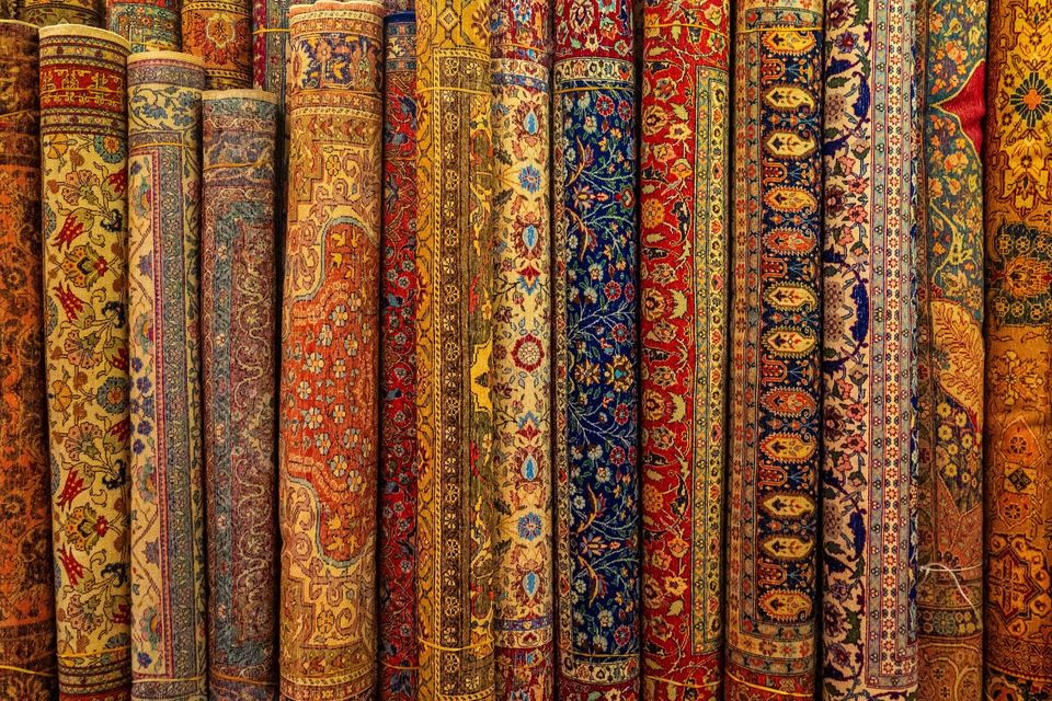 Inside a rug store, rolled and folded rugs displayed in wooden shelving.