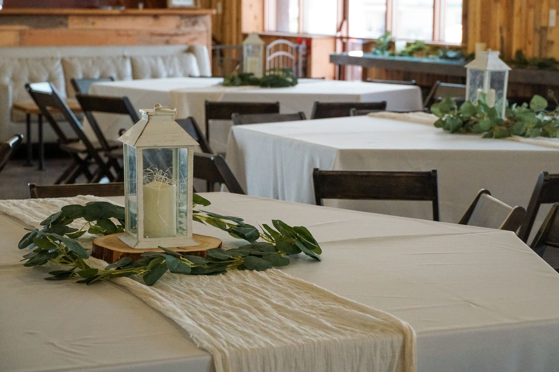 A white lantern with a candle inside of it is sitting on a wooden table.