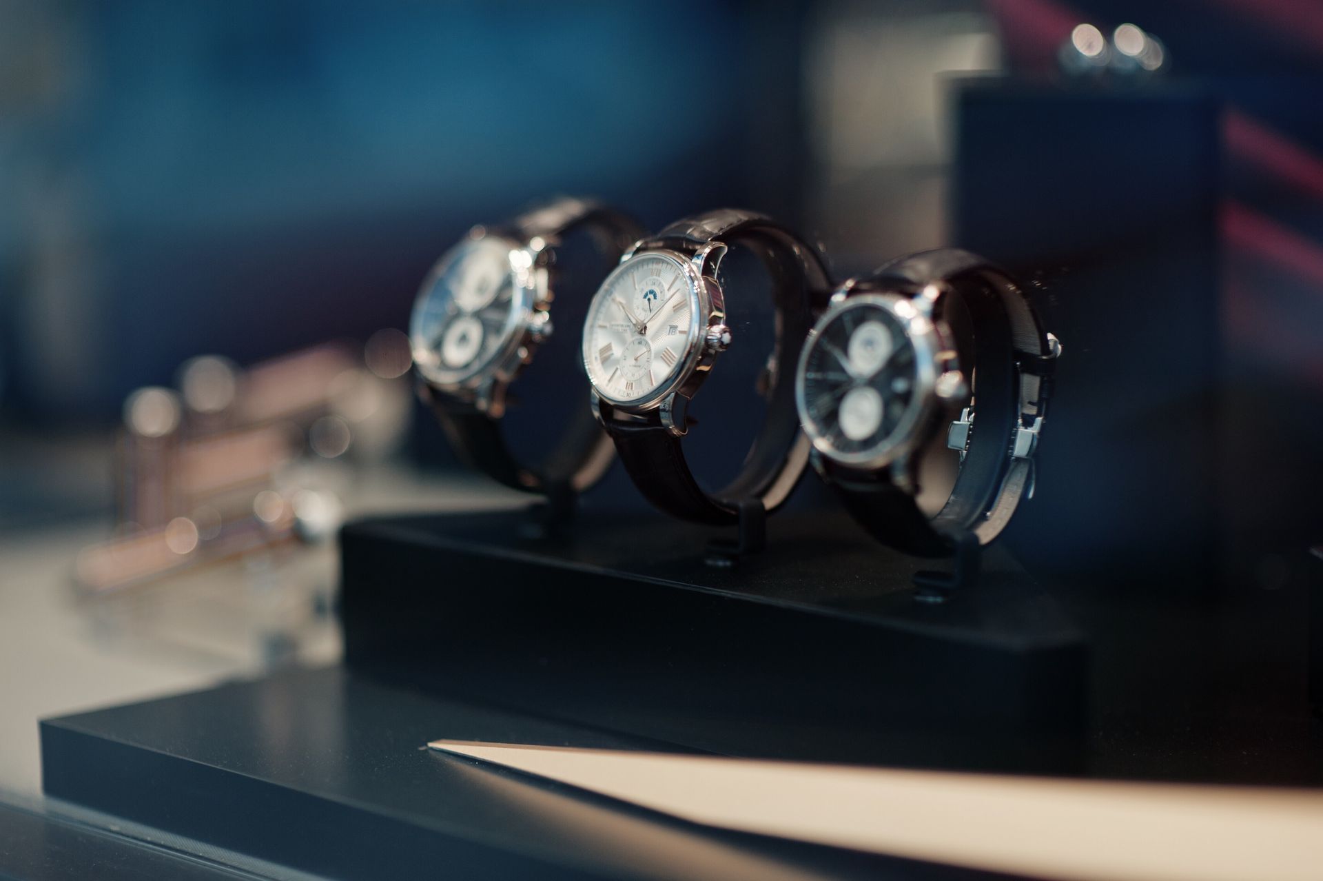 Three luxury wristwatches with leather straps on a display stand.