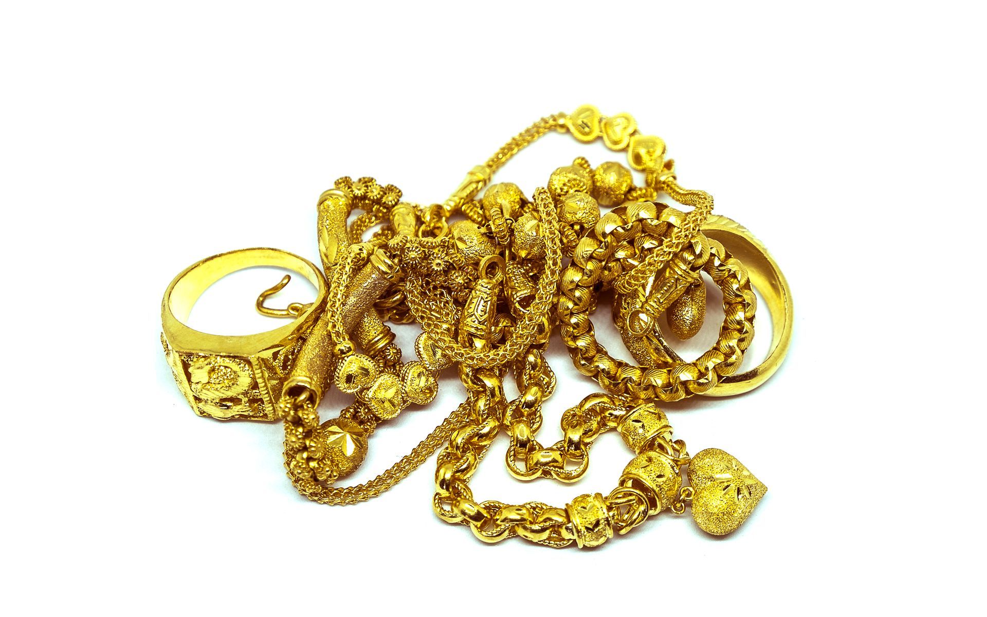 Gold jewelry pile: necklaces, rings on white background.