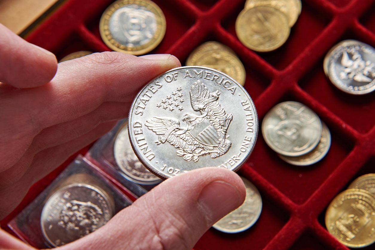 Hand holding silver coin with eagle design, set of coins in red velvet tray.