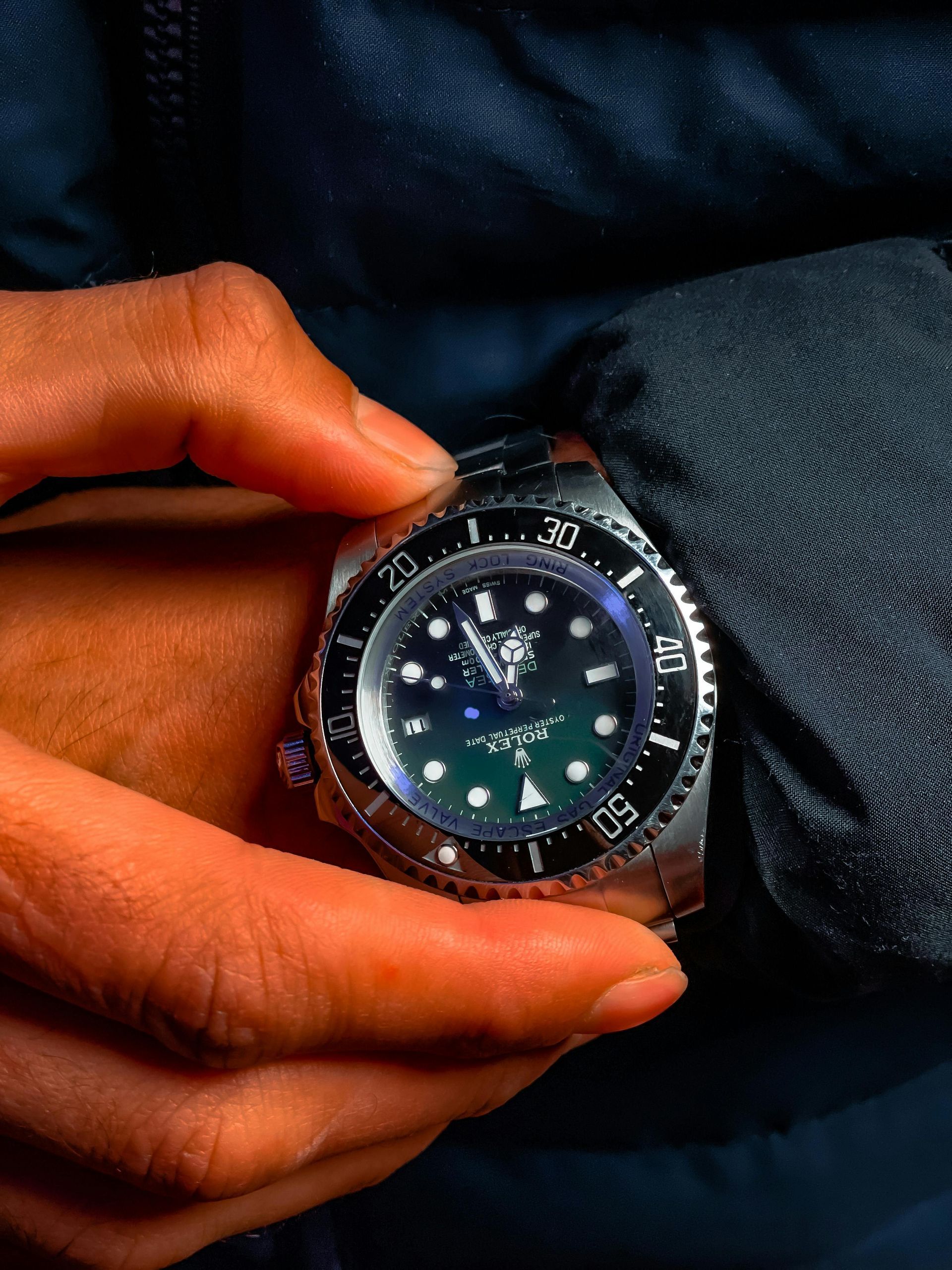 Person wearing a silver wristwatch with a black bezel and dark blue/green face.
