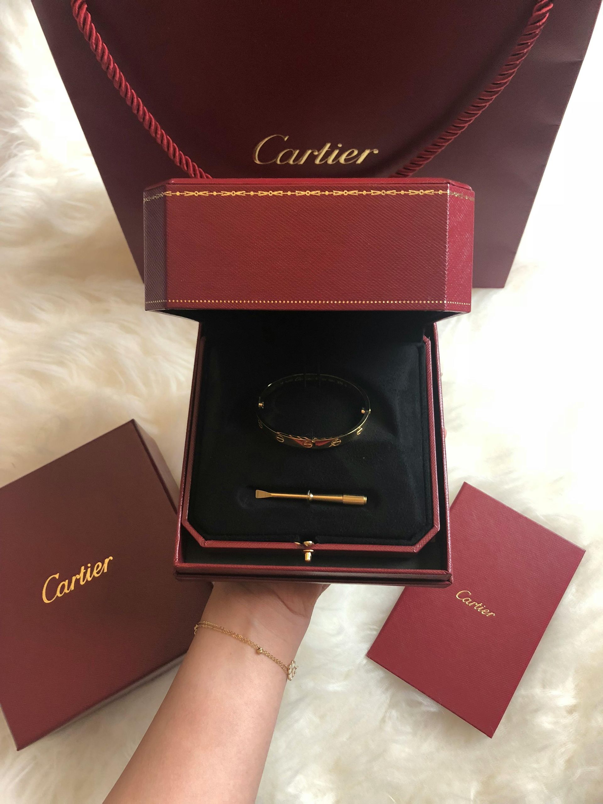Cartier bracelet in red box, with shopping bag and small boxes on white fur.