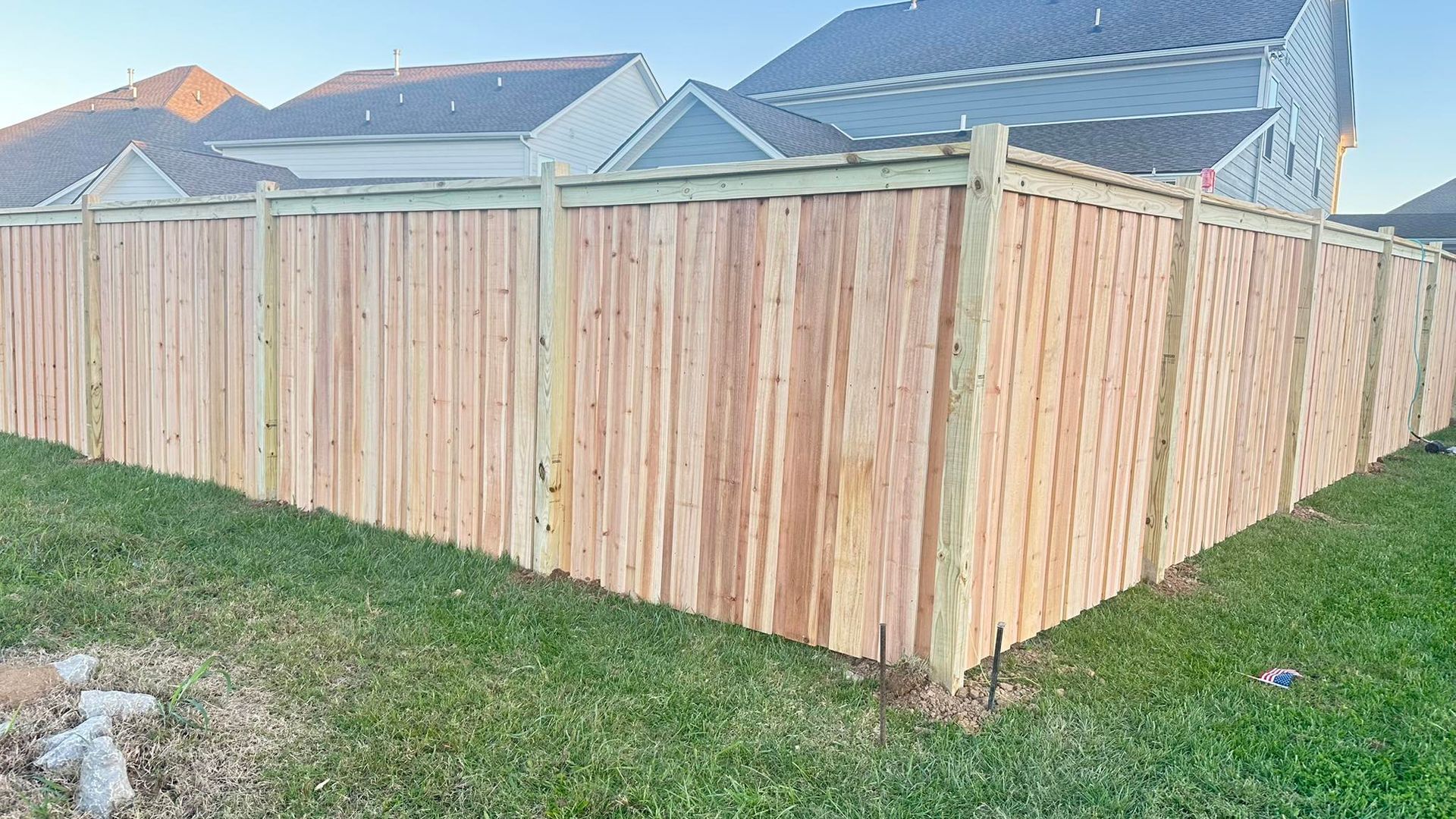 Wooden privacy fence with a corner gate beside a grassy yard and suburban houses.