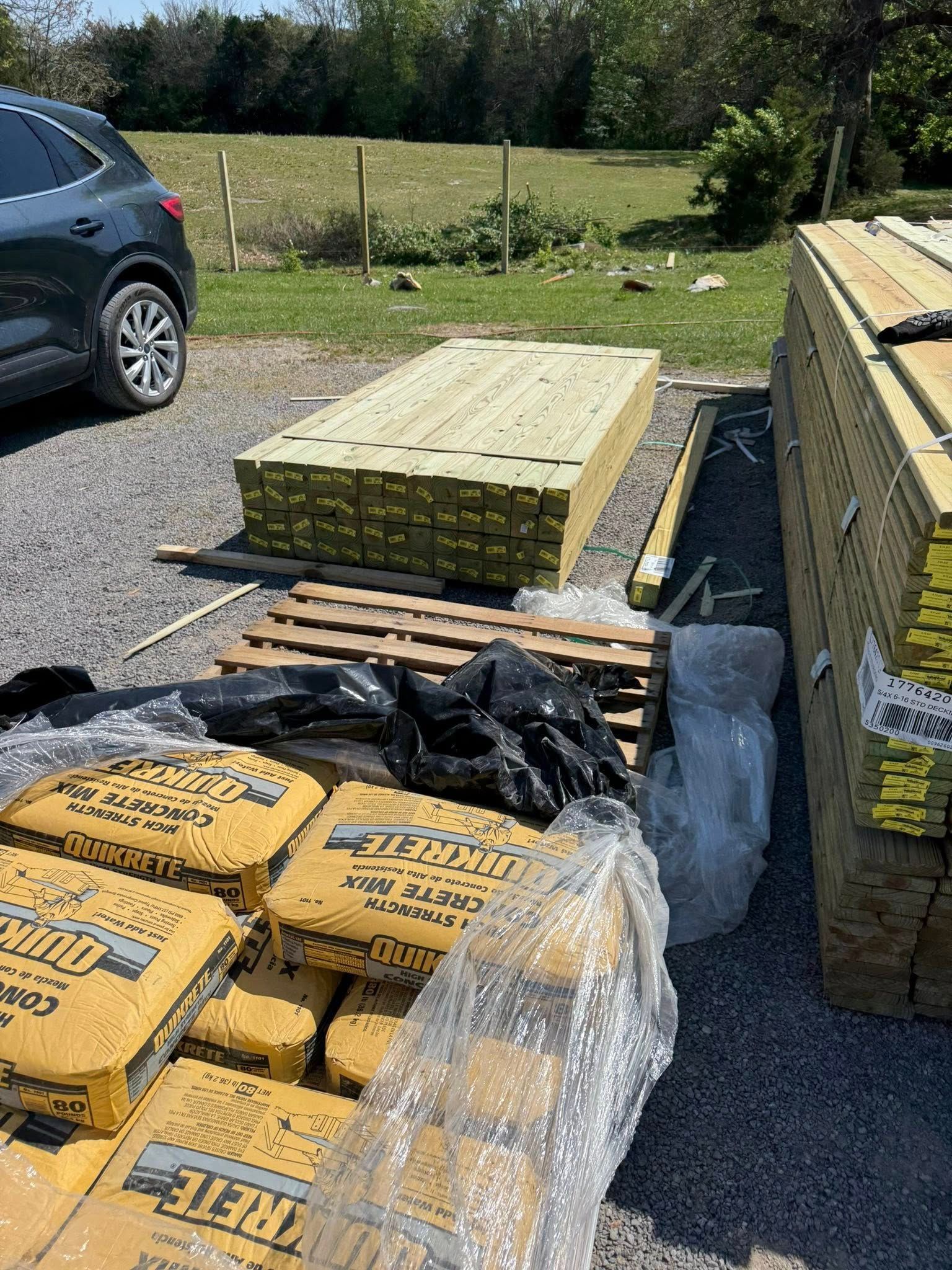 Stacked construction materials and gravel bags beside a parked car in a yard.