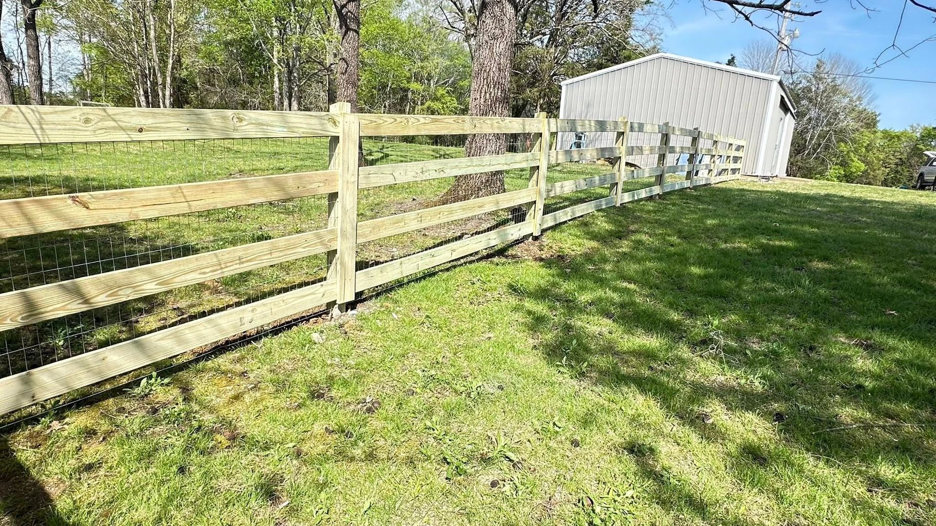Wooden fence beside a grassy yard, with trees and a small white shed in the background.